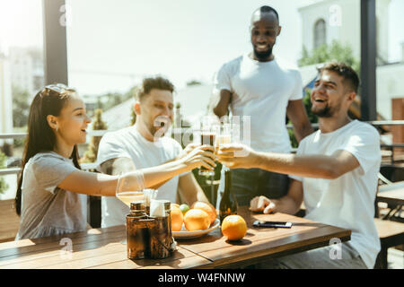 Young group of friends drinking beer, having fun, laughting and celebrating together. Women and men with beer's glasses in sunny day. Oktoberfest, friendship, togetherness, happiness, summer concept. Stock Photo