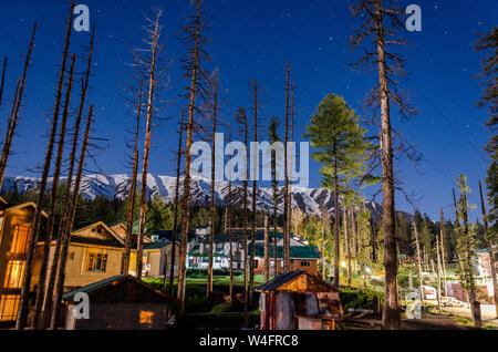 Nocturnal view of snow capped Pir Panjal Range looking over houses and hotels amidst pine trees at Gulmarg, Jammu and Kashmir, India Stock Photo