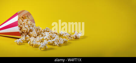 striped cone bag with spilled popcorn on yellow background with copy space Stock Photo