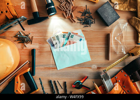 Money in envelope on carpentry woodwork workshop desk, top view Stock Photo