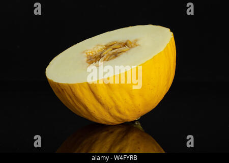 One half of fresh yellow melon canary isolated on black glass Stock Photo