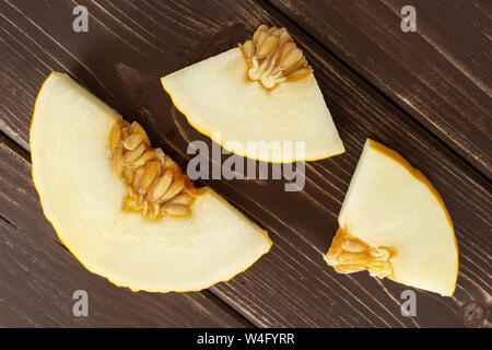 Group of one slice two pieces of fresh yellow melon canary flatlay on brown wood Stock Photo