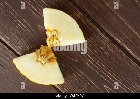 Group of two pieces of fresh yellow melon canary copyspace on right flatlay on brown wood Stock Photo