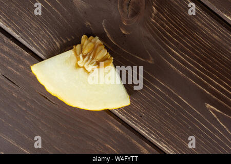 One piece of fresh yellow melon canary flatlay on brown wood Stock Photo