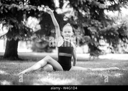 Girl gymnast sits in a pose of twine on the lawn in the park. Black and white image. Stock Photo