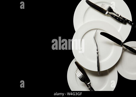 top view of white round plates with cutlery isolated on black with copy space Stock Photo