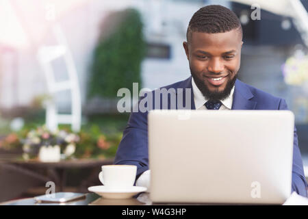 Smiling African American Businessman Working On Laptop In Outdoor Cafe Stock Photo