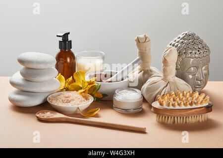 spa cosmetics, stones, massage brush, candle, Buddha figurine on beige surface isolated on grey Stock Photo