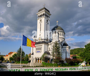 Holy Trinity orthodox church in Sighisoara, with flying Romanian flag in front, and message on wall in green Stock Photo