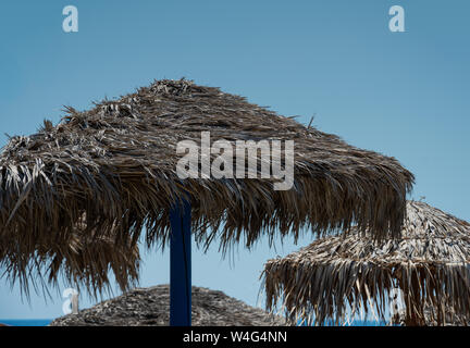 Parasols on the beach of Perissa, their cover made of dried palm leaves Stock Photo