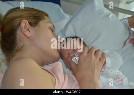 A mother kissing her newborn baby sleep in bed at a hospital. Stock Photo