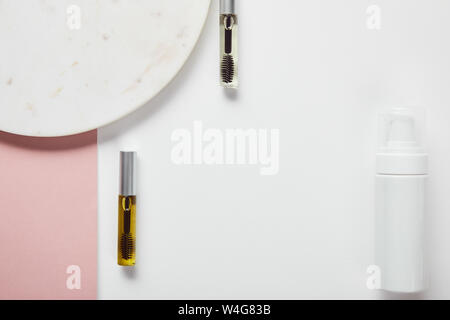 top view of mascara bottles and cosmetic dispenser near plate on white pink surface Stock Photo