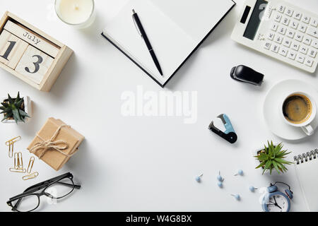 top view of wooden calendar, notepad, pen, glasses, plants, coffee and office supplies on white surface Stock Photo