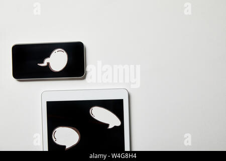 digital tablet and smartphone with paper thought and speech bubbles on white surface Stock Photo