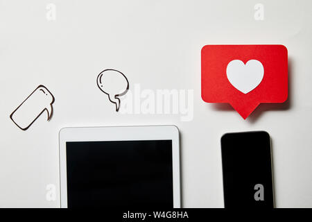digital tablet and smartphone with paper thought and speech bubbles, paper heart, like card on white surface Stock Photo