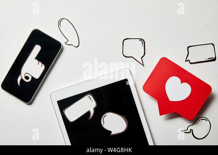 digital tablet and smartphone with paper thought and speech bubbles, paper heart, pointing card on white surface Stock Photo