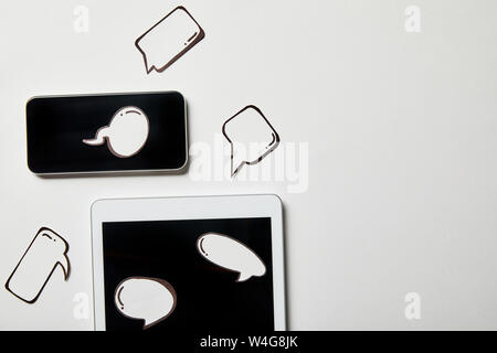 digital tablet and smartphone with paper thought and speech bubbles on white surface Stock Photo