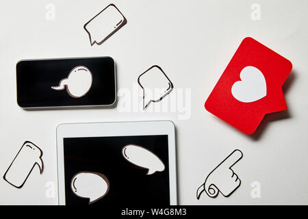 digital tablet and smartphone with paper thought and speech bubbles, paper heart, pointing card on white surface Stock Photo