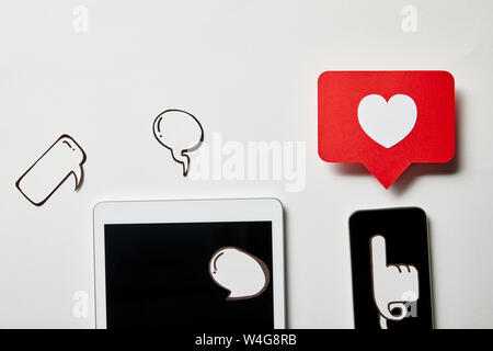 digital tablet and smartphone with paper thought and speech bubbles, paper heart, pointing card on white surface Stock Photo