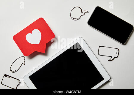 smartphone near digital tablet with like sign card, paper thought and speech bubbles on white surface Stock Photo