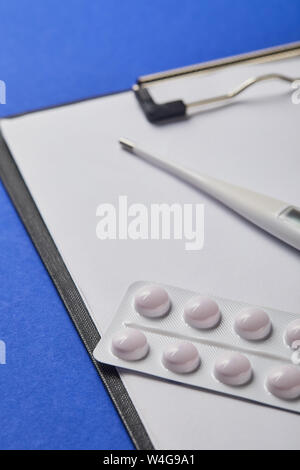 selective focus of blister pack and thermometer on folder with blank paper isolated on blue Stock Photo