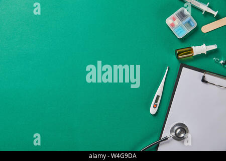 syringe, wooden tongue depressor, ampule, pill box, nasal spray, thermometer, stethoscope and folder on green background Stock Photo