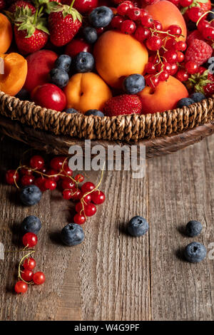 close up view of ripe berries and apricots in wicker basket on wooden table Stock Photo
