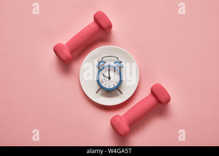 top view of dumbbells and plate with toy alarm clock on pink background Stock Photo
