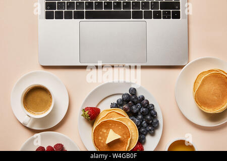 top view of tasty breakfast with pancakes, berries, cup of coffee and honey near laptop Stock Photo