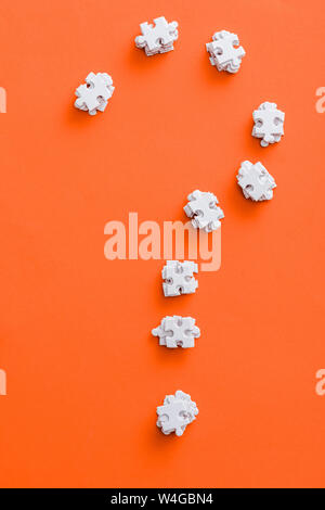 top view of question mark shape with white puzzle pieces on orange Stock Photo