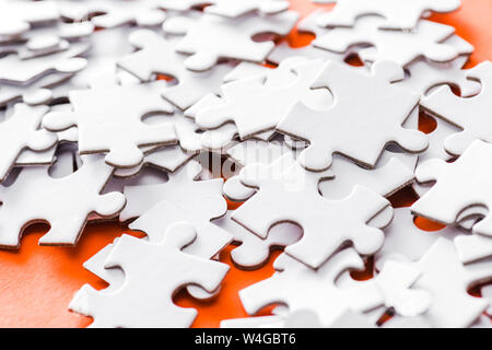 selective focus of incomplete white jigsaw puzzle pieces on orange Stock Photo