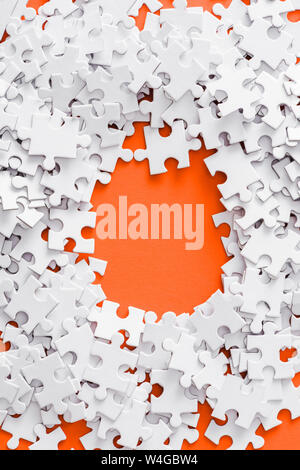 top view of pile with white jigsaw puzzle pieces on orange Stock Photo