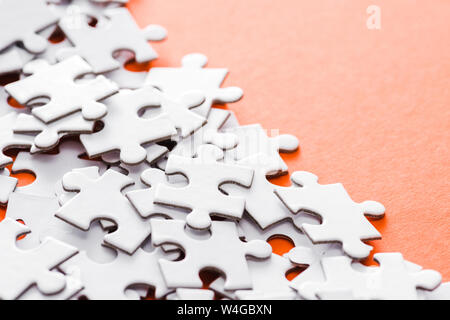 selective focus of unfinished white jigsaw puzzle pieces on orange Stock Photo