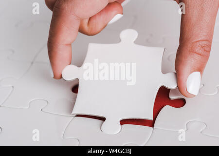 close up of woman holding white jigsaw near connected puzzle pieces Stock Photo