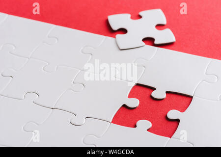 selective focus of unfinished white puzzles near separate piece isolated on red Stock Photo