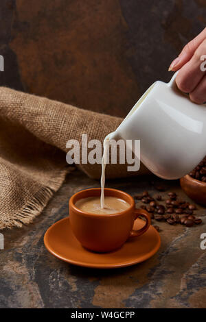 cropped view of woman pouring milk in cup with coffee on marble table Stock Photo