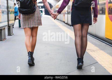 Back view of two women with backpacks walking hand in hand on platform, Porto, Portugal Stock Photo