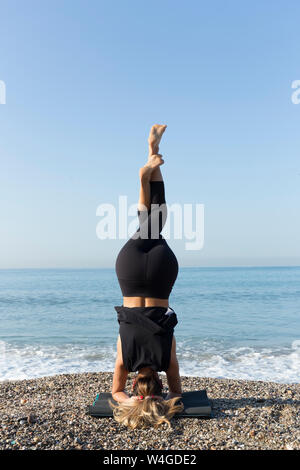 Young woman practicing yoga on the beach, doing headstand Stock Photo