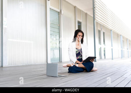 Female balett dancer sitting on the ground, using tablet and laptop Stock Photo