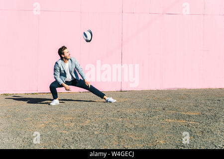 Young man in front of pink construction barrier, watching his hat flying in the wind Stock Photo