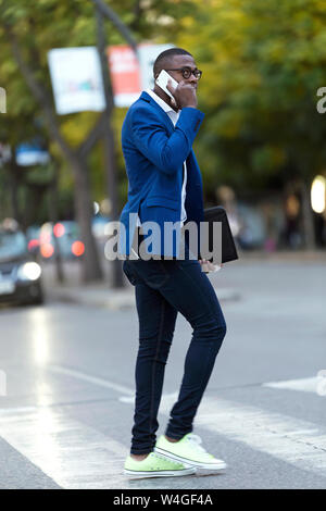 Young businessman wearing blue suit jacket crossing the road and using smartphone Stock Photo