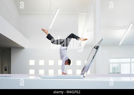 Businessman doing a handstand at laptop in office Stock Photo
