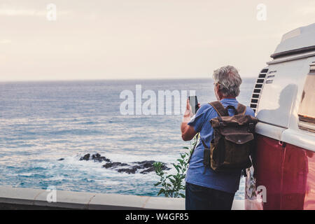 Senior man travelling in a vinatge van, using smartphone, rear view Stock Photo