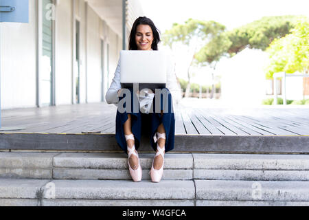 Female ballet dancer using laptop sitting on steps Stock Photo