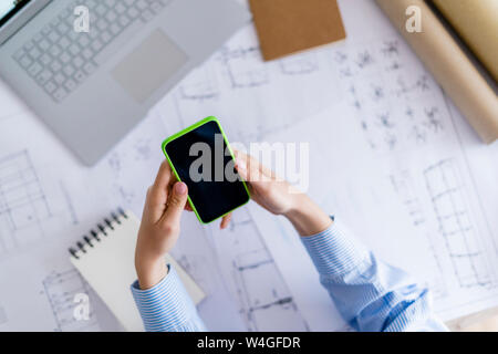 Close-up of woman in office using cell phone with blueprint on table Stock Photo