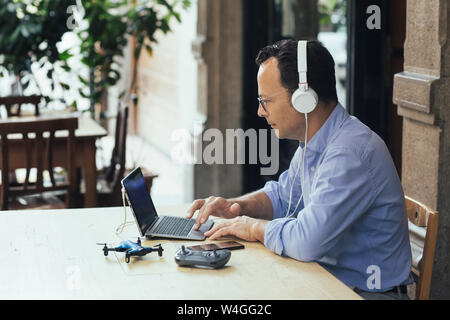 Businessman with headphones, laptop and drone in a coffee shop Stock Photo