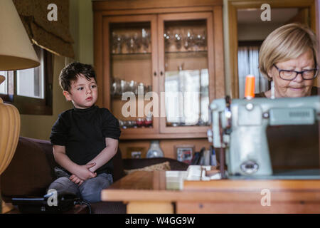 Grandmother using an old sewing machine watched by her grandson Stock Photo