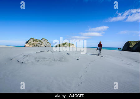 Woman walking in the white sand dunes on Wharariki Beach, South Island, New Zealand Stock Photo