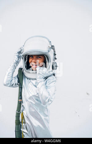 Portrait of laughing little girl wearing space suit and space hat in front of white background Stock Photo