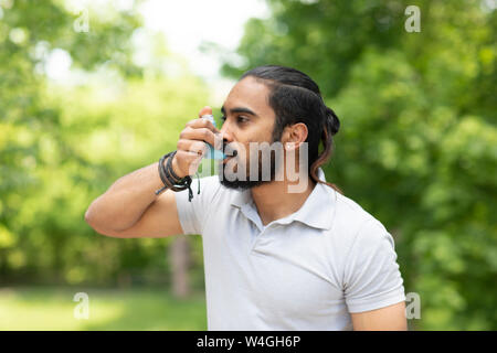 Young man in nature using asthma inhaler Stock Photo
